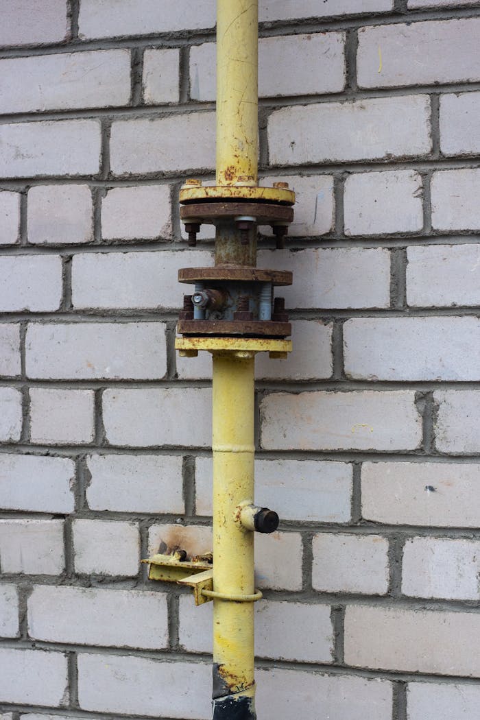 Close-up view of a rusty yellow metal pipe attached to a brick wall outdoors.